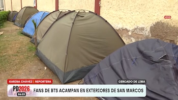Varias carpas de campaña de distintos colores alineadas sobre el césped junto a un muro exterior