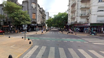 Vista de calle de la intersección de Calles 12 y 58 en La Plata, con edificios de varias plantas, tiendas, árboles, coches aparcados y peatones