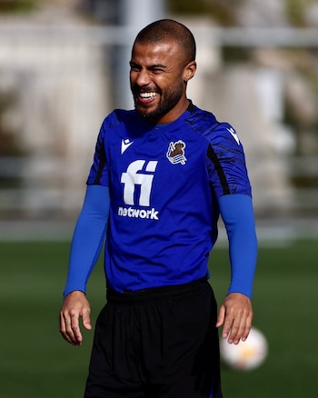 Close do jogador do Real Sociedad Carlos Vinicius com camisa azul de manga comprida sorrindo e olhando para a esquerda no campo de futebol