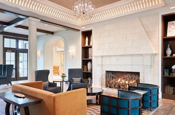 Interior de un lujoso lobby de hotel con una chimenea encendida, sofás naranjas, sillones grises y azules, y una araña de cristal en el techo