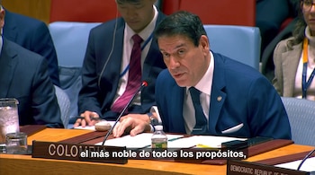 Un hombre con traje azul y corbata habla frente a un micrófono en una mesa con una placa que dice Colombia.