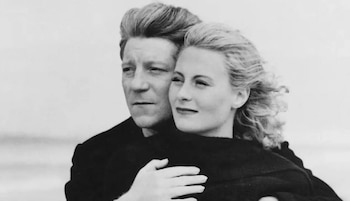 Una fotografía en blanco y negro de un hombre y una mujer. El hombre mira a la izquierda y la mujer a la derecha, su cabeza recostada sobre su hombro. Él la abraza por la cintura