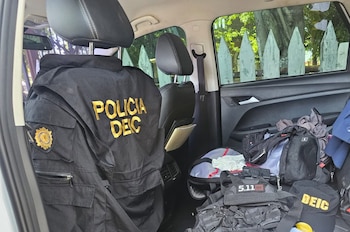 Dos agentes uniformados de la Policía Nacional Civil caminan junto a tres hombres vestidos de civil por un camino de tierra