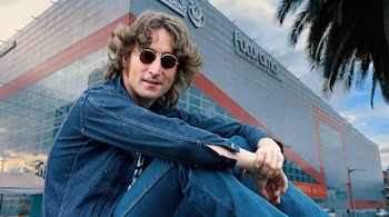 John Lennon sentado con chaqueta de mezclilla y gafas de sol redondas delante del edificio del Centro Cultural Futurama.