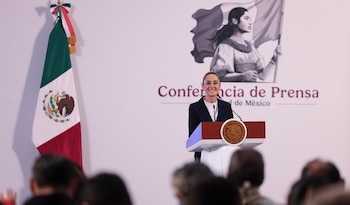 Claudia Sheinbaum Pardo sonríe en un podio con el escudo de México, frente a una bandera mexicana y un fondo blanco con 'Conferencia de Prensa'
