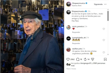 Retrato de Julio Le Parc, un hombre mayor con gorra oscura y traje a rayas, posando frente a una instalación artística de paneles reflectantes
