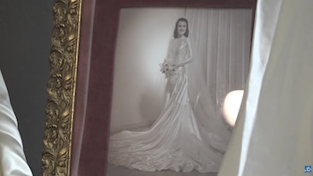 Fotografía en blanco y negro enmarcada de una mujer sonriente con un vestido de novia de satén de manga larga, velo y un ramo, con un marco dorado ornamental