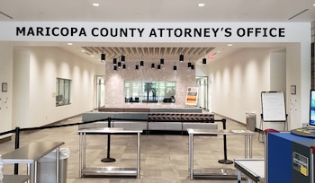 Vestíbulo con el letrero Maricopa County Attorney's Office, barreras de seguridad de cinta negra, mesas metálicas y sillones