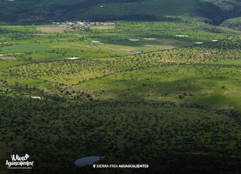 Vista aérea de un paisaje verde con colinas, zonas de vegetación densa, campos, varios cuerpos de agua y un pequeño pueblo a lo lejos