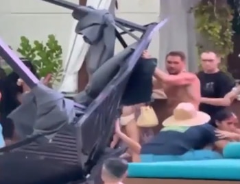 Varias personas observan una estructura oscura colapsada en un área exterior. Se distinguen individuos, incluyendo uno sin camisa y otro con sombrero