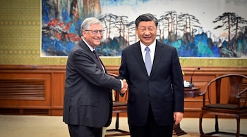 Dos hombres, Bill Gates y Xi Jinping, se dan la mano en una sala con un gran cuadro abstracto y mobiliario de madera.