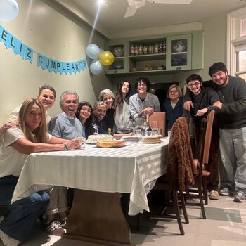 Jairo y un grupo de nueve personas posan sonrientes alrededor de una mesa con postres, bajo una pancarta de 'Feliz Cumpleaños' y globos en un interior