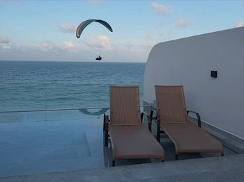 Dos reposeras frente a una piscina de borde infinito con vista al océano y una persona en parapente en el cielo