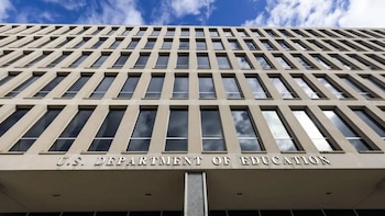 Edificio de varios pisos del Departamento de Educación de EE. UU. con una fachada beige y múltiples ventanas rectangulares que reflejan el cielo azul y nubes