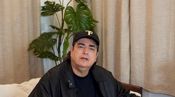 Jaime Bayly viste gorra y chaqueta negra mientras habla sentado en un interior con cortinas y una planta de fondo