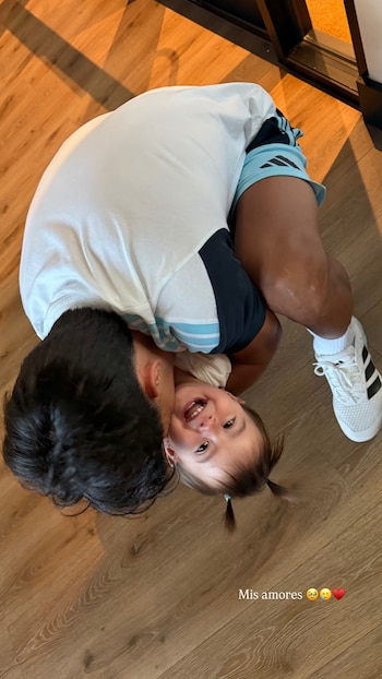 Desde arriba, Lisandro Martínez, de espaldas, abraza a su hija Muri López Benítez, quien sonríe feliz a la cámara en un suelo de madera