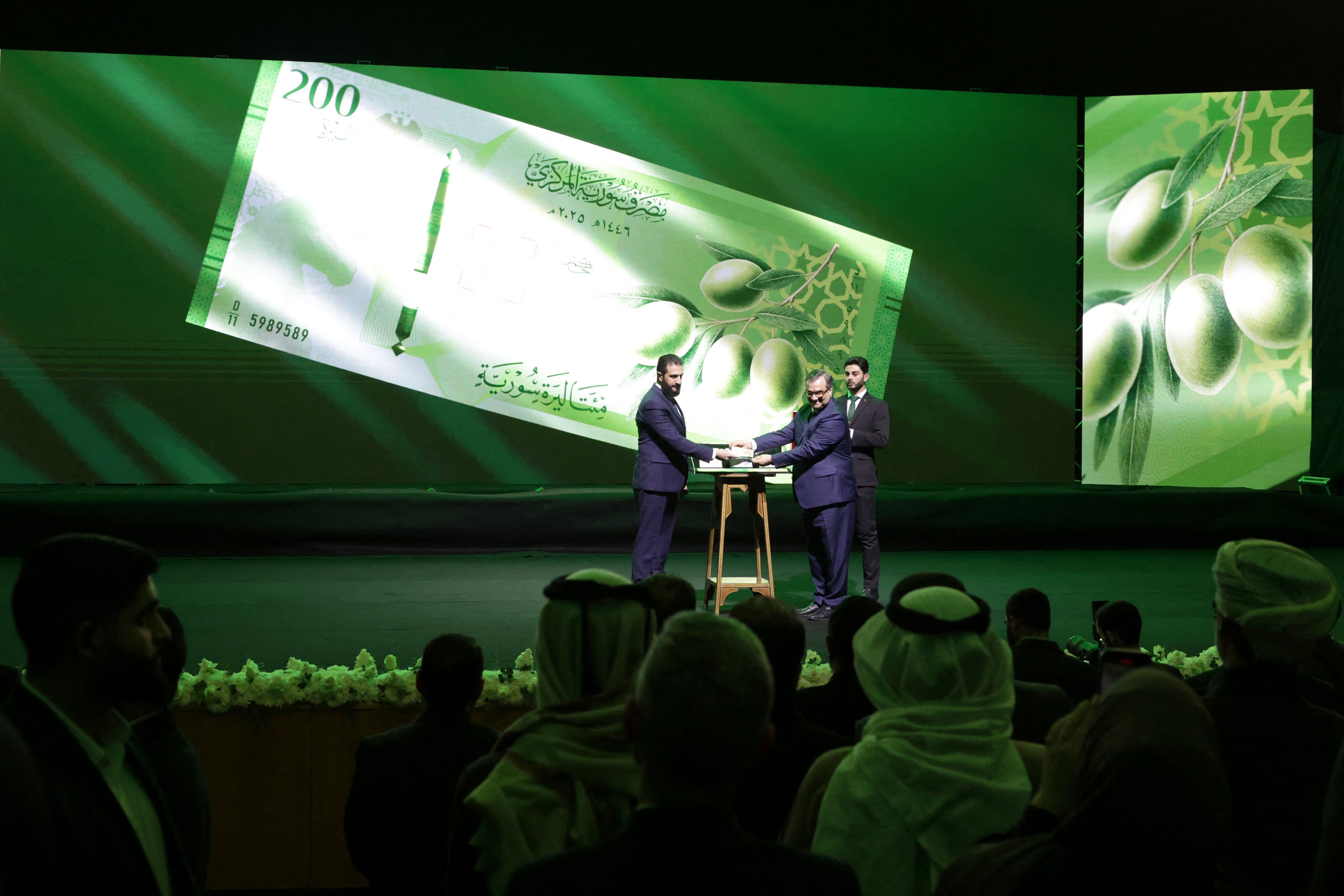 El presidente de Siria, Ahmed al-Sharaa, y el jefe del Banco Central, Abdul Qadir al-Hasriya, muestran uno de los nuevos billetes del país durante la presentación oficial en Damasco (Bakr ALkasem / AFP)