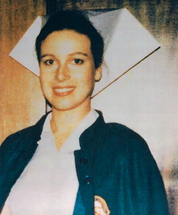 Mujer joven de cabello oscuro sonríe, viste cofia de enfermera blanca, camisa blanca y chaqueta oscura con insignia
