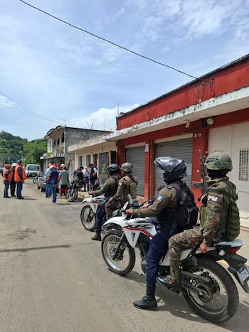 Un grupo de personas con chalecos naranjas, cascos de seguridad y gorras observa un mapa extendido en una calle