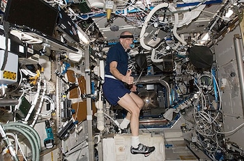 Astronauta con ropa deportiva e instrumental médico hace ejercicio en un módulo interior cubierto de cables y paneles técnicos