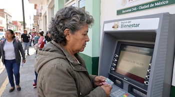 Mujer con chaqueta verde inserta tarjeta en cajero automático gris de Banco del Bienestar, con pantalla que muestra "Pensión Mujeres Bienestar" y "Consulta de saldo".