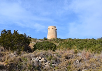 Una torre de piedra clara sobre el monte de vegetación y el cielo azul con nubes ligeras.