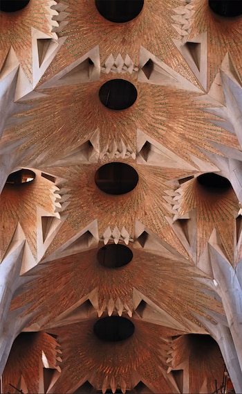Primer plano del techo de la Sagrada Familia, mostrando múltiples bóvedas hiperbólicas con patrones radiales en tonos naranja y verde, y aberturas circulares oscuras