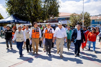 Un grupo de autoridades y funcionarios con chalecos de emergencia camina al aire libre en la plaza de una localidad