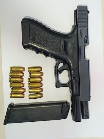 Una pistola negra con la corredera abierta, un cargador suelto y doce balas ordenadas en dos columnas sobre una superficie blanca