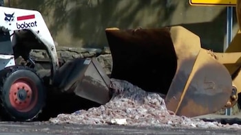Una cargadora compacta blanca Bobcat y el cucharón de una máquina amarilla remueven una pila de desechos sobre el suelo