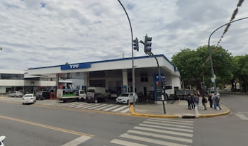 Vista exterior de una estación de servicio YPF en una esquina urbana de Rosario, con bombas de combustible, vehículos, un paso de cebra y semáforos