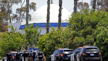 Vista parcial del Centro Islámico de San Diego con cúpula blanca y techo azul, rodeado de árboles. Varios coches y agentes de policía visibles en primer plano