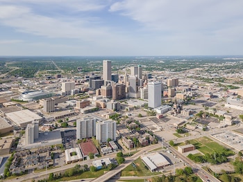 Vista aérea de Oklahoma City. El distrito centro presenta rascacielos como la Torre BOK. Se ven carreteras, áreas verdes y edificios, bajo un cielo azul con nubes