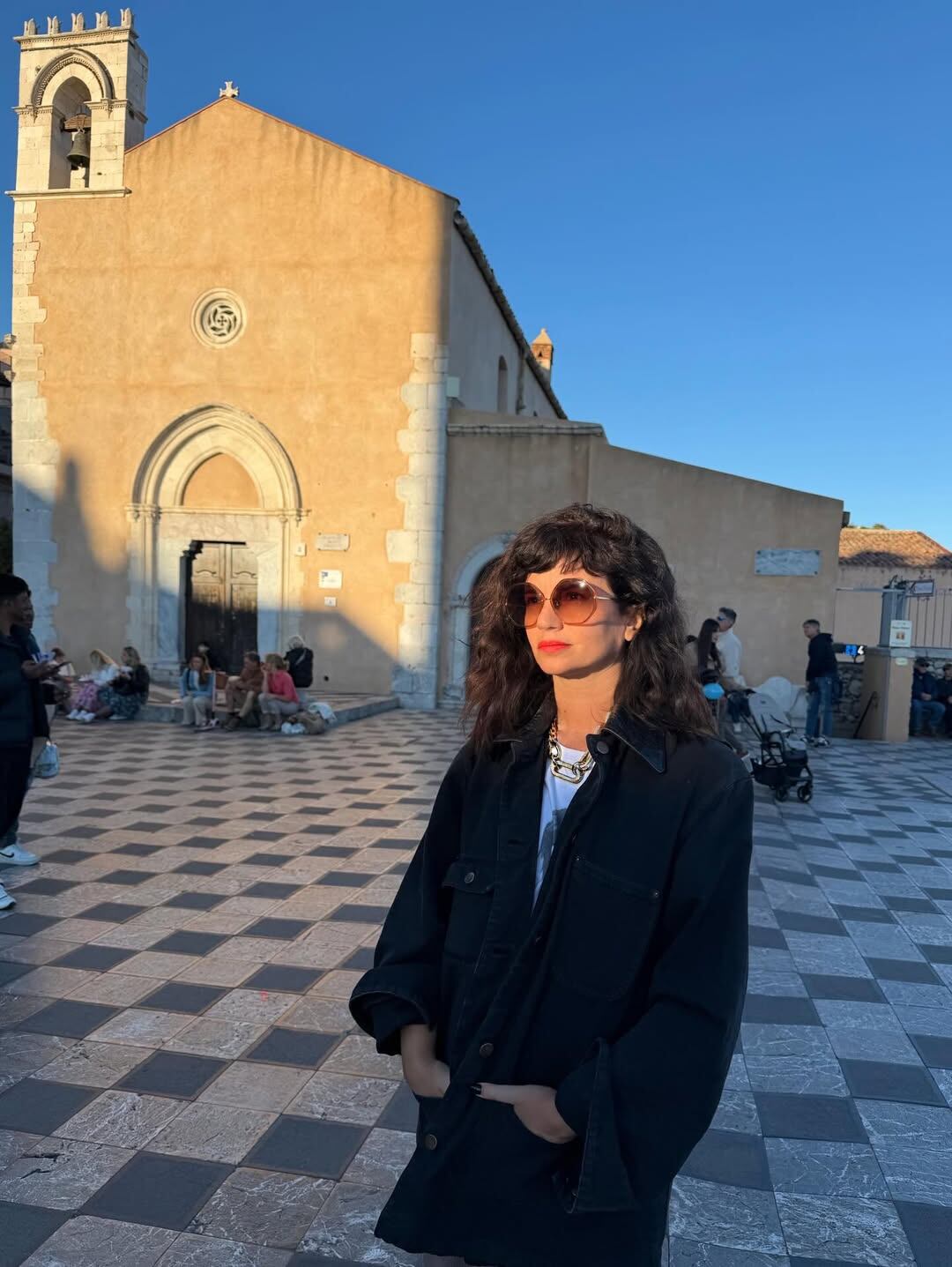 Con un look casual y gafas de sol, con una antigua iglesia en el fondo bajo la luz dorada del atardecer