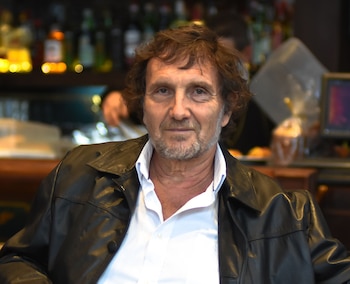 Retrato de Juano Villafañe, un hombre de cabello castaño con chaqueta de cuero negra y camisa blanca, en un café