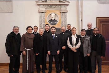 Once personas, la mayoría con sotanas o atuendos clericales, posan sonrientes en una sala con un busto de mármol en la pared