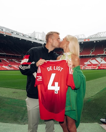 Un hombre y una mujer se besan y sostienen una camiseta roja de fútbol con el dorsal cuatro en el campo de un estadio