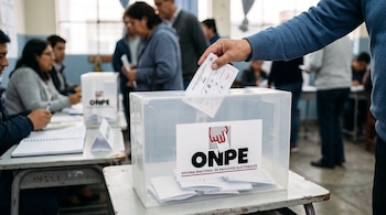 Una mano introduce una cédula de votación en una urna transparente con el logotipo de la ONPE colocada sobre una mesa.