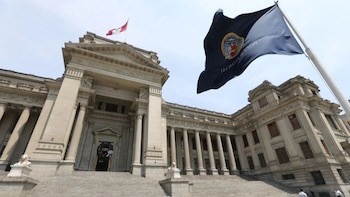 Edificio de piedra estilo neoclásico con columnas y escalinatas, bandera azul del Poder Judicial de Perú y bandera nacional, bajo cielo despejado