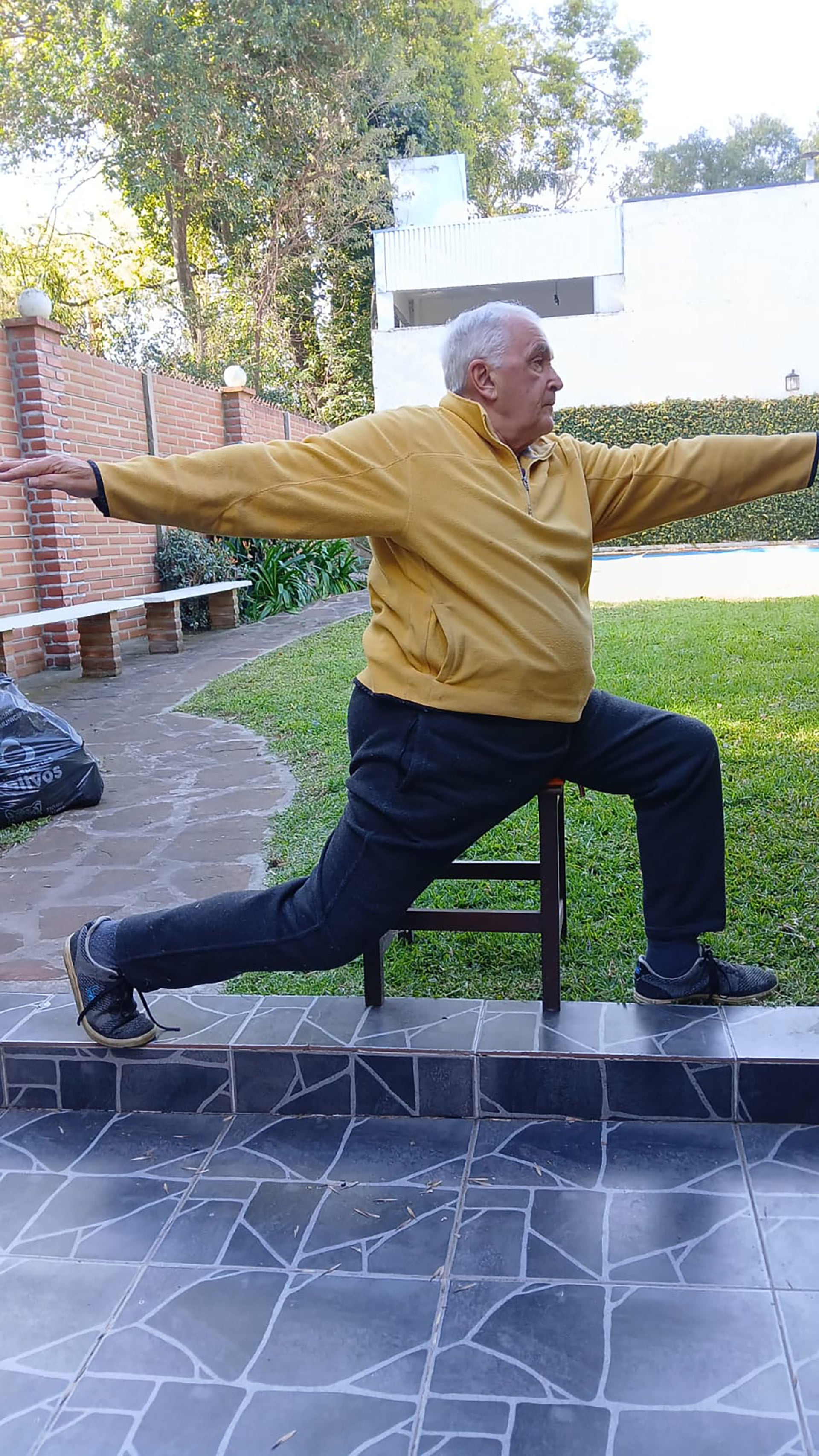 Eduardo García, practicando yoga en silla en el jardín de su casa