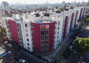 Vista aérea de un edificio de apartamentos blanco y rojo en una zona urbana, con vehículos aparcados en la calle y la ciudad al fondo