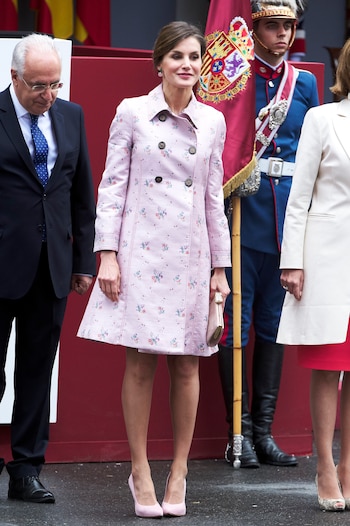 El desfile de 2018 se celebró en Logroño, donde Letizia recuperó una pieza nueva de su armario, un vestido-abrigó que estrenó un mes antes. Firmado por Carolina Herrera, este diseño era de color rosa, con estampado floral y silueta evasé.
Los complementos de ese día fueron unos altos salones rosas de Lodi y unos pendientes de Coolook, hechos de plata cubierta de oro champán, aventurina verde y cuarzo rosa.