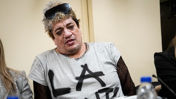 Pity Álvarez viste una camiseta gris con letras escritas, mangas de red y gafas de sol negras sobre la cabeza