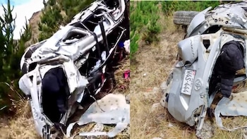 Un vehículo gris destruido y volcado sobre un terreno inclinado con pasto seco, con la placa de Perú visible en la parte trasera