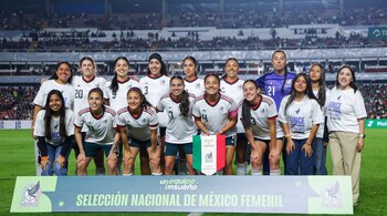 Jugadoras de fútbol con uniforme blanco posan alineadas en una cancha tras una pancarta de la selección mexicana.