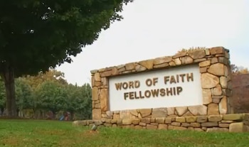 Un letrero de piedra en un césped verde muestra el texto Word of Faith Fellowship junto a un grupo de árboles