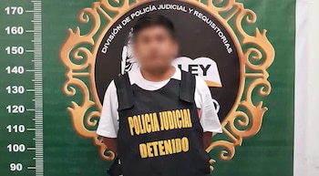 Un hombre con el rostro difuminado viste un chaleco negro con la frase POLICIA JUDICIAL DETENIDO frente a un fondo con escala de estatura