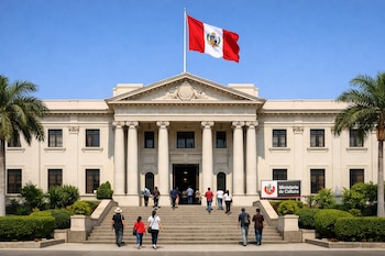 Fachada de museo con columnas, escalinata, bandera peruana, personas, palmeras y cartel del Ministerio de Cultura bajo cielo azul despejado.