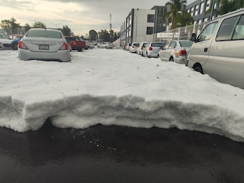Vista de un estacionamiento y una calle cubiertos por una gruesa capa de granizo blanco, con varios coches estacionados semienterrados en la nieve