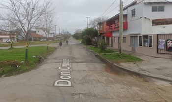 Una calle residencial en Mar del Plata llamada Don Orione, con casas bajas, árboles sin hojas, césped y dos personas caminando en la distancia bajo un cielo nublado